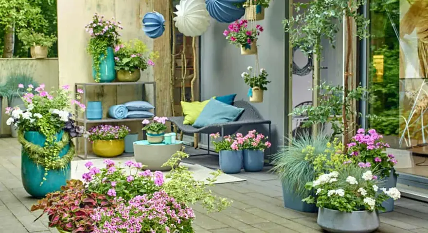 Bunte Blumen und grüne Pflanzen auf einer Terrasse, mit Hängekörben und Kissen. Tolle gartendeko ideen für Ihr Zuhause.