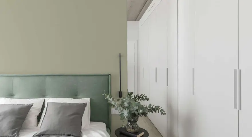 Ein Schlafzimmer mit einer Wand in hellem Olivgrün und einem Bett mit grünem Kopfteil. Der Unterschied zwischen Khaki und Oliv ist hier subtil, aber präsent.