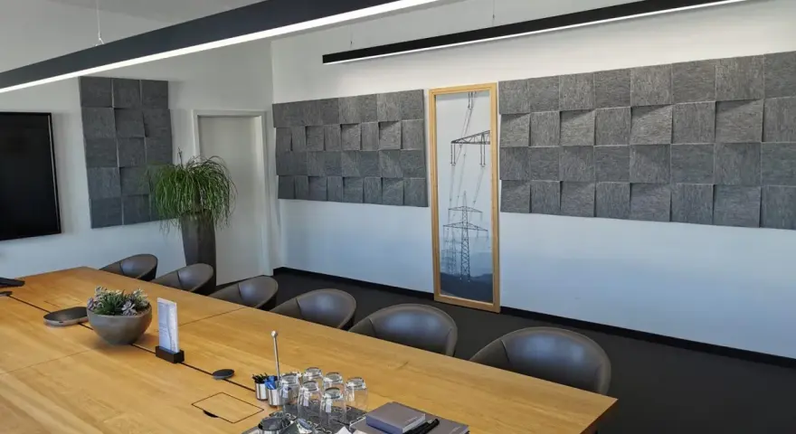 Moderne Konferenzraumgestaltung mit Akustikpaneelen an der Wand, um den **Schall im Raum zu reduzieren**. Ein großer Holztisch mit Gläsern und Notizbüchern steht im Vordergrund.