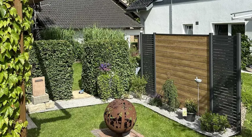 Schöner Garten mit Hecken und Holzzaun als Sichtschutz. Eine Feuerkugel und Pflanzen schaffen Gemütlichkeit. Tolle Ideen für Sichtschutz im Garten.
