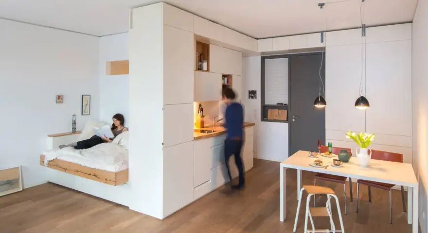 Clevere raumaufteilung ideen: Ein Bettbereich ist vom Wohnbereich durch eine weiße Wand getrennt. Eine Küche und ein Essbereich sind integriert.