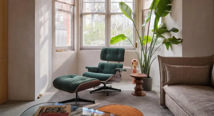 Gemütliches mid century wohnzimmer mit einem dunkelgrünen Sessel und Hocker, einer großen Zimmerpflanze und einem beigefarbenen Sofa.