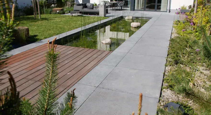 Moderner Vorgarten gestalten: Teich, Holzdeck und Sitzbereich laden zum Entspannen ein. Grüne Rasenflächen und blühende Pflanzen schaffen eine harmonische Atmosphäre.