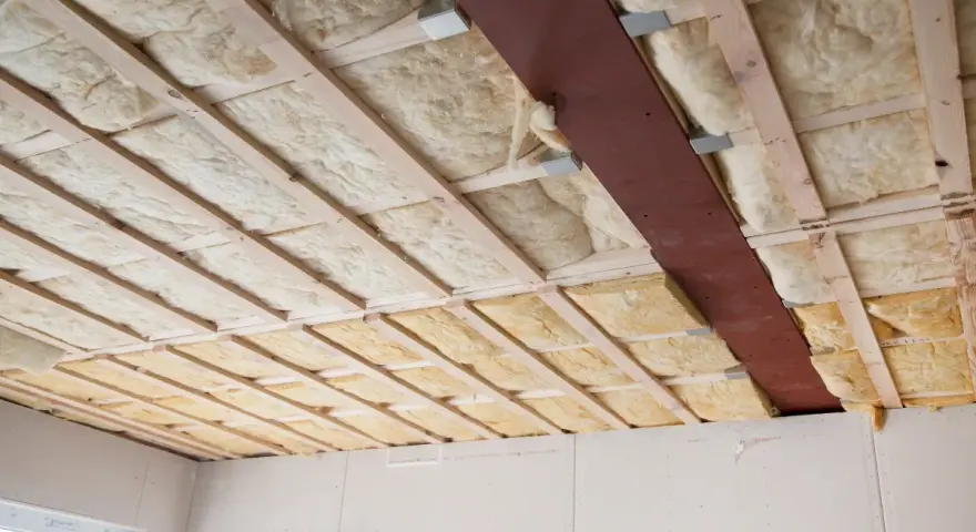 Decke mit Holzbalken und Dämmung. Hier sieht man, was ist Glaswolle: ein isolierendes Material, das in Hohlräume eingebracht wird.