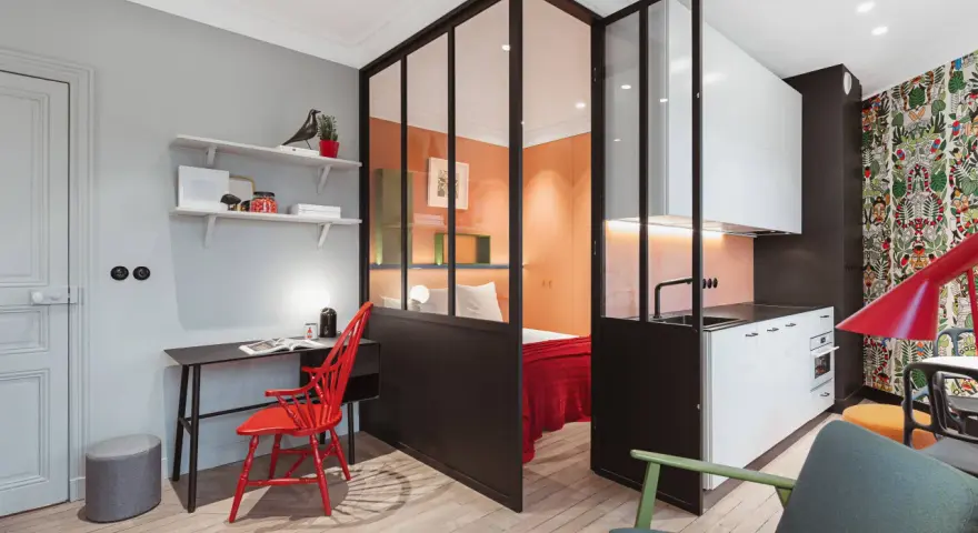 Clever 35 qm wohnung einrichten: Schlafbereich, Küche und Arbeitsplatz sind durch Glaswände getrennt. Bunte Akzente wie der rote Stuhl und die Tapete beleben den Raum.