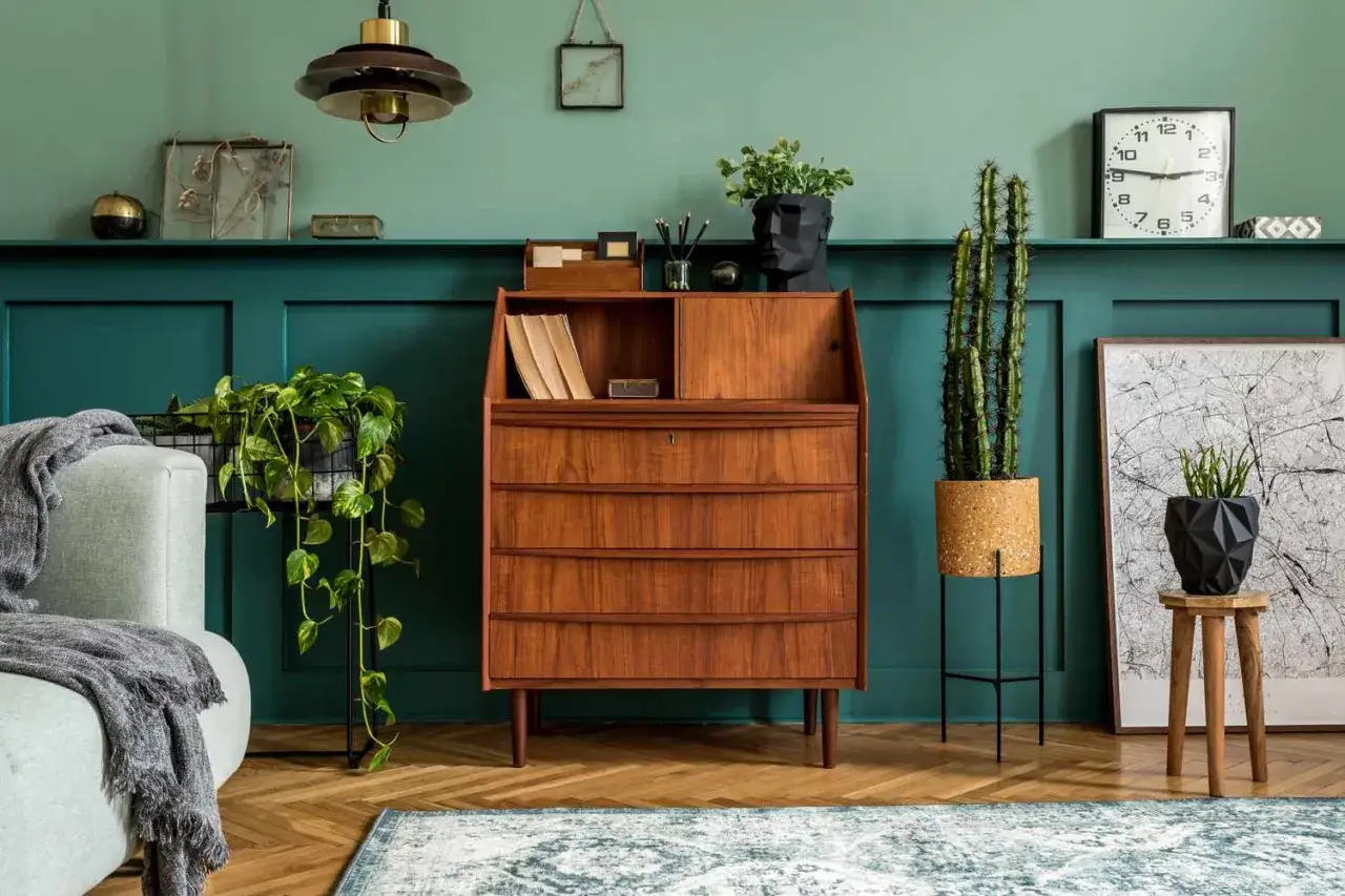Ein Mid-Century-Schreibtisch aus Holz und eine Wand in tiefem T&uuml;rkis. Pflanzen und Deko-Objekte setzen Akzente, um Holz und Farben zu kombinieren.