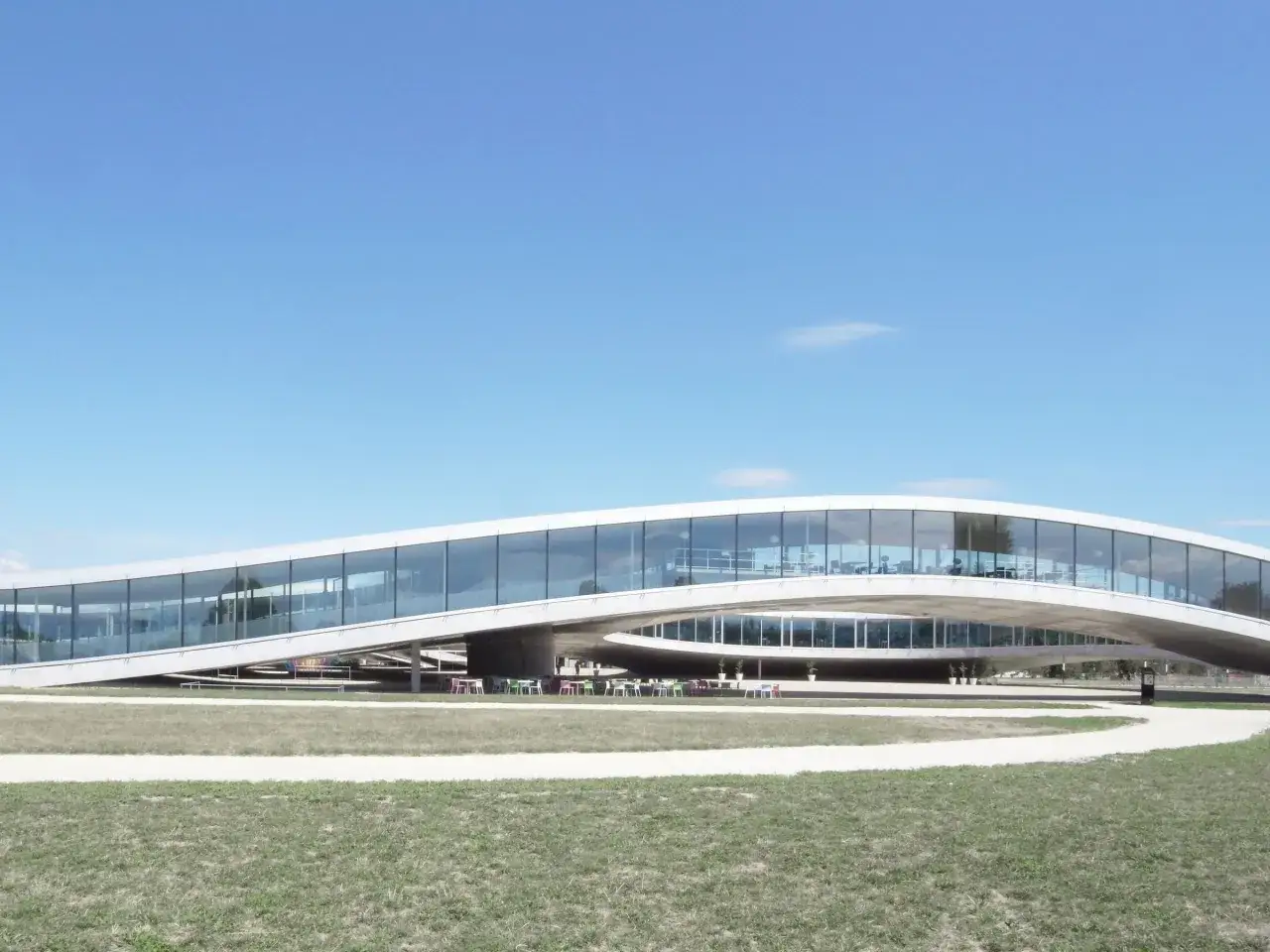 Das moderne, geschwungene Geb&auml;ude des Rolex Learning Center mit viel Glas und einer gr&uuml;nen Au&szlig;enanlage.
