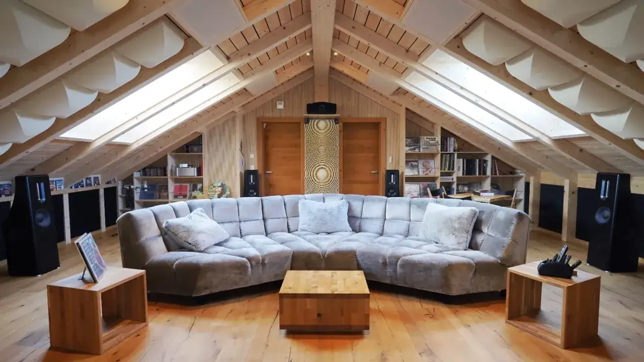 Gem&uuml;tliches Wohnzimmer mit schallabsorbierenden Elementen an der Decke, die helfen, den Schall im Raum zu reduzieren. Gro&szlig;e Couch, Lautsprecher und B&uuml;cherregale.