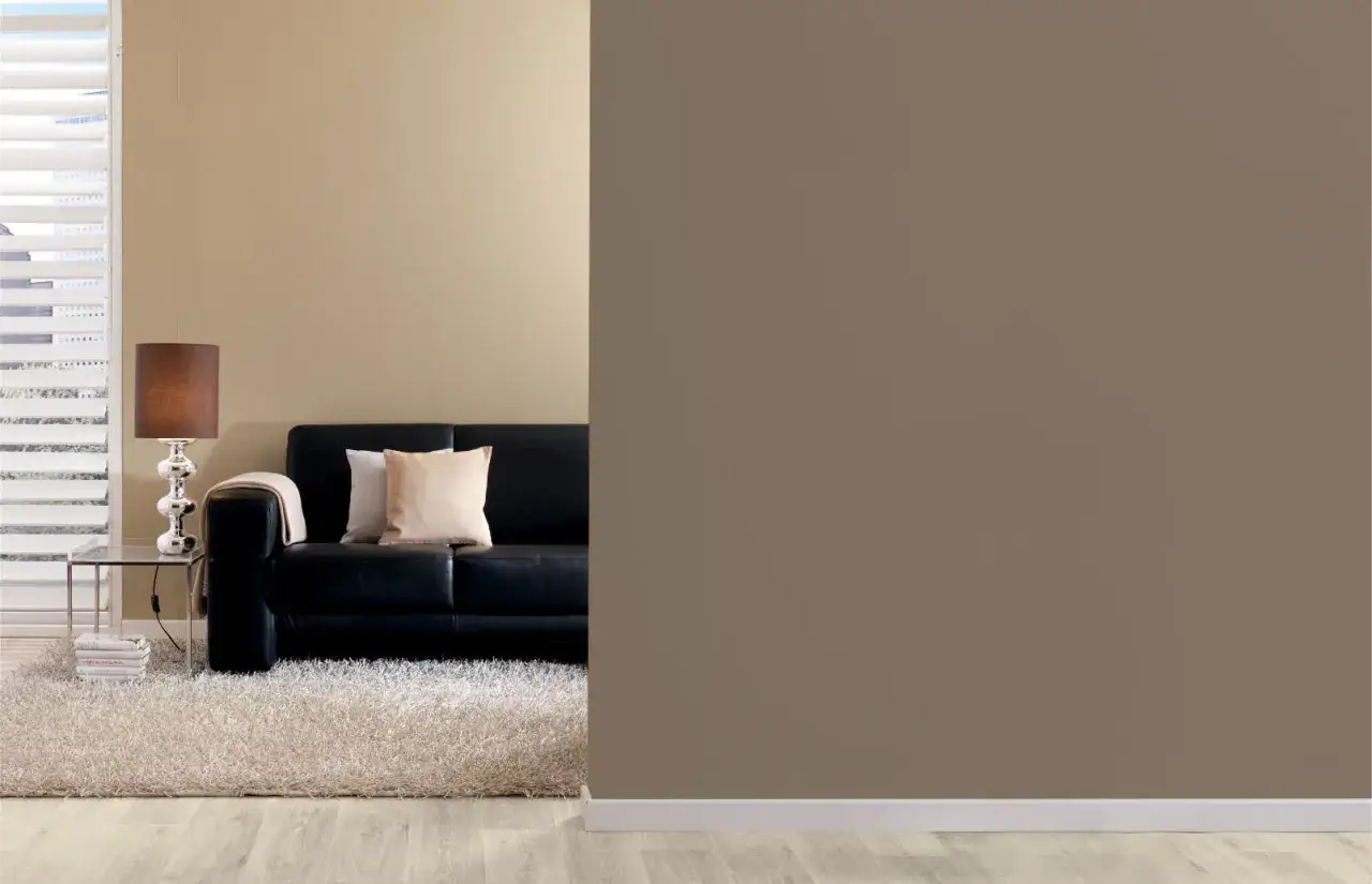 Schwarzes Ledersofa mit Kissen und Decke, daneben ein Beistelltisch mit Lampe. Der Teppich und die Wandfarbe mischen sich in warmen Braunt&ouml;nen.