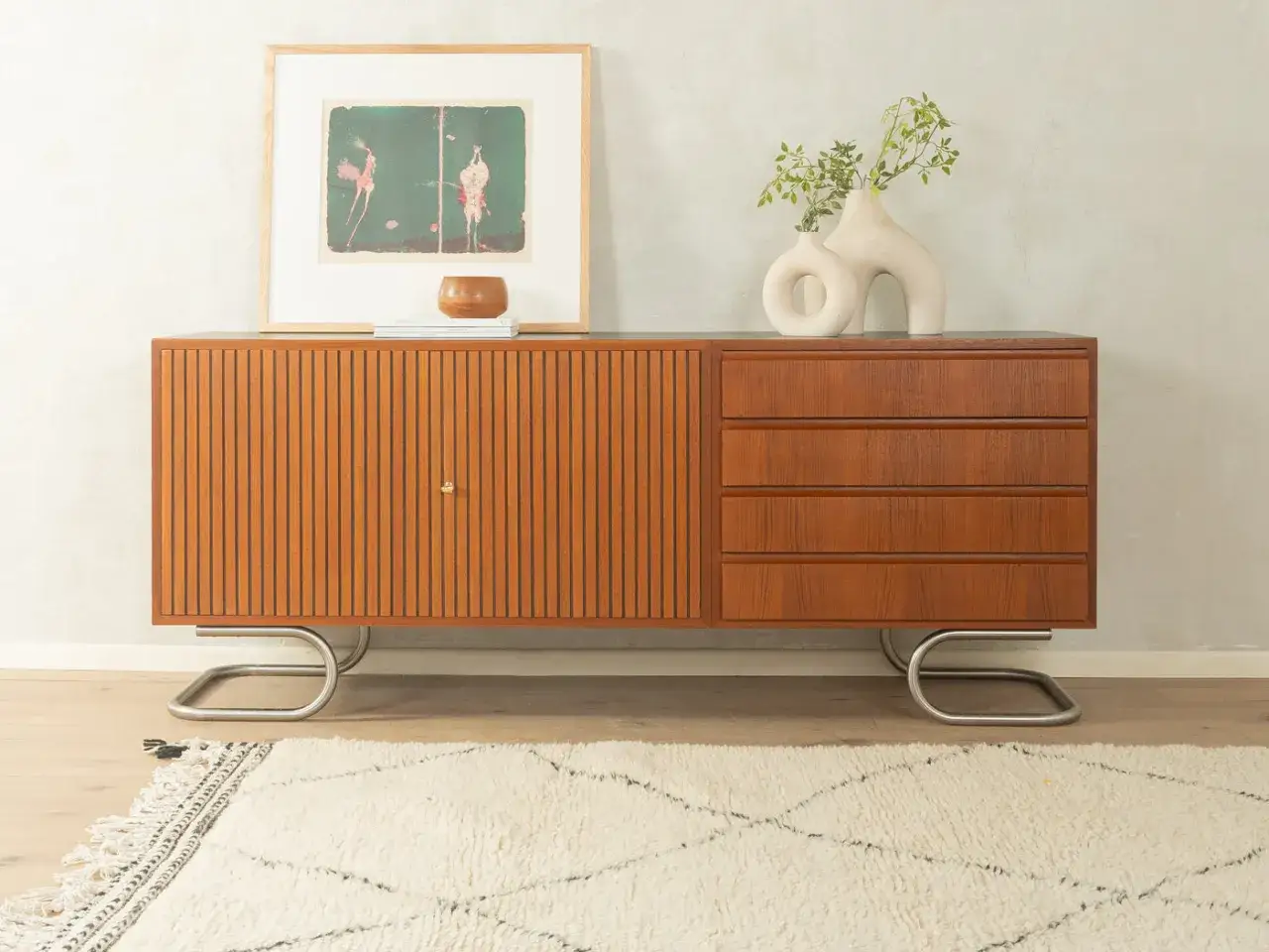Stilvolles Mid Century Wohnzimmer mit einem Sideboard aus Teakholz, gerippten T&uuml;ren und Schubladen, darauf ein Bild und Vasen.