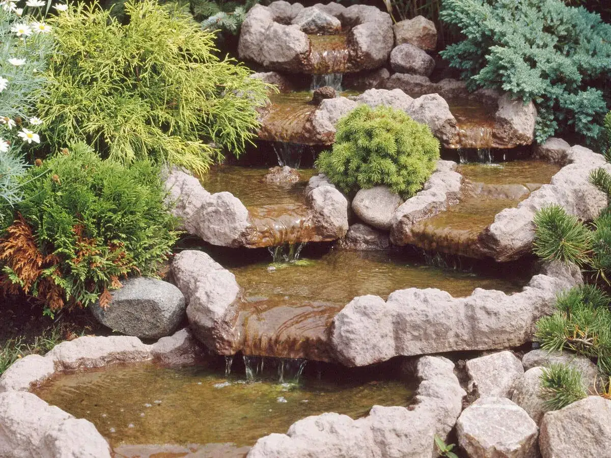 Nat&uuml;rliche Bachlauf Garten Ideen mit kleinen Kaskaden und &uuml;ppiger Bepflanzung. Steine und Wasser erzeugen eine beruhigende Atmosph&auml;re.