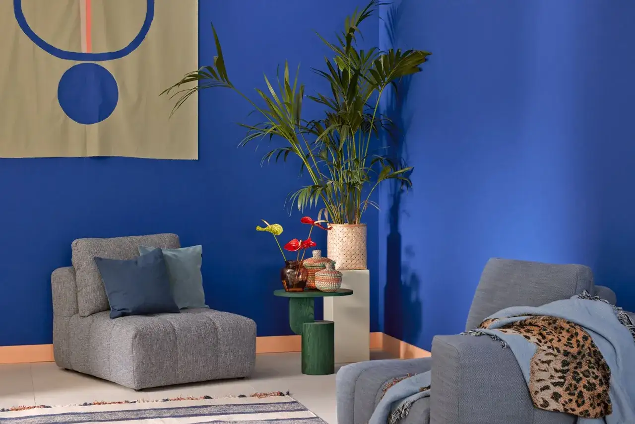 Graue Sessel und ein Teppich mit Streifen bilden einen schönen Kontrast zur kobaltblauen Wand. Welche Farbe passt zu dunkelblau? Hier: Beige, Orange und Grün.