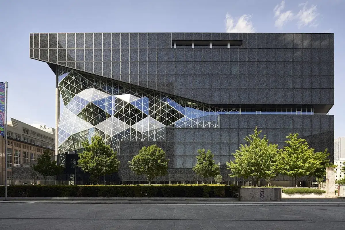 Der Axel Springer Neubau in Berlin mit seiner markanten Glasfassade und dunklen Au&szlig;enh&uuml;lle, umgeben von B&auml;umen.