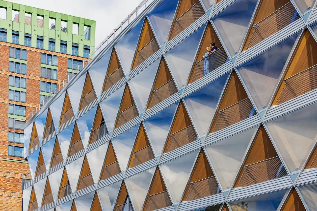 Moderne Fassade mit dreieckigen Fenstern, die das Cradle to Cradle Prinzip verk&ouml;rpert. Zwei Personen genie&szlig;en die Aussicht.
