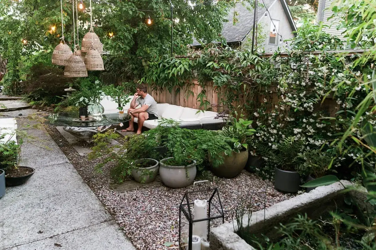 Mann entspannt im gr&uuml;nen Garten, der skandinavisch gestaltet ist. H&auml;ngende K&ouml;rbe und Lichterketten schaffen Gem&uuml;tlichkeit.