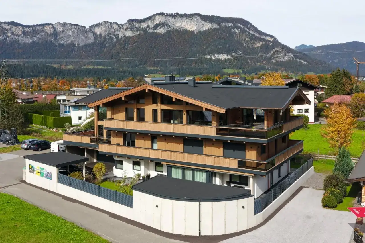 Modernes Holzhaus mit Balkonen und Bergkulisse im Herbst.
