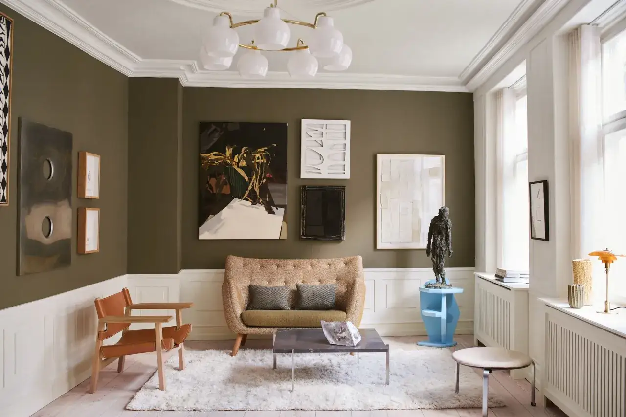 Gem&uuml;tliches Wohnzimmer mit Kunst an den W&auml;nden, einem beigen Sofa und einem Ledersessel. Warme Farben dominieren den Raum, der durch eine weiche Decke und ein stilvolles Ambiente besticht.