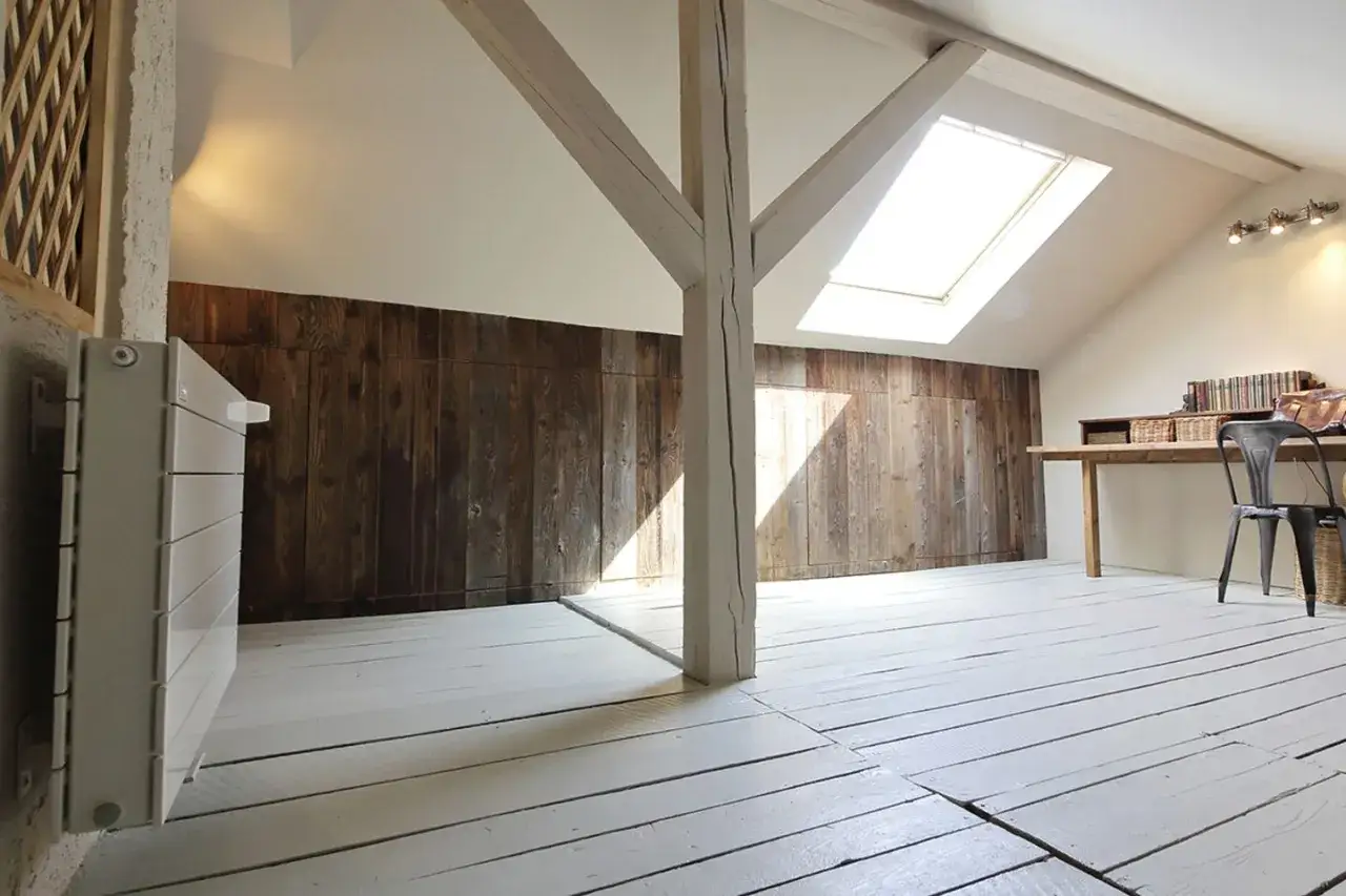 Ein heller Dachboden mit Holzwand und wei&szlig;em Boden, ideal f&uuml;r ein nachhaltig saniertes Zuhause.