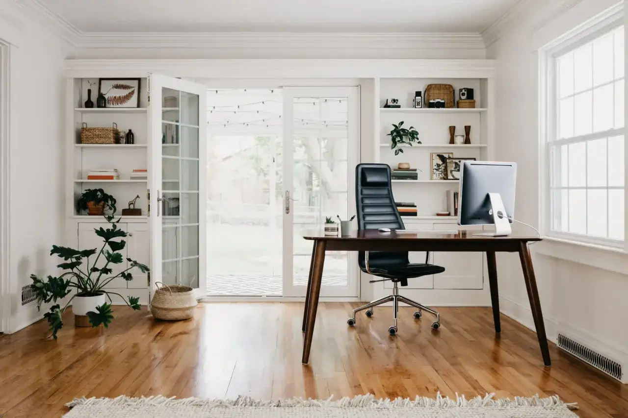 Ein stilvolles B&uuml;ro mit Schreibtisch, Computer und einem ergonomischen Design-Stuhl. Ein gro&szlig;er Topfpflanze und B&uuml;cherregale schm&uuml;cken den Raum.