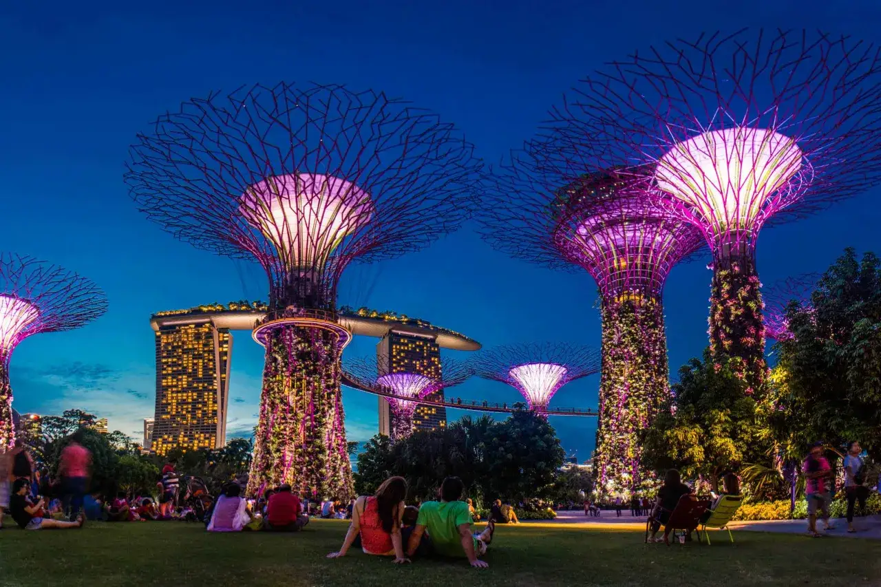 Abendliche Szene in den Gardens by the Bay mit leuchtenden Supertrees und dem Marina Bay Sands Hotel im Hintergrund.