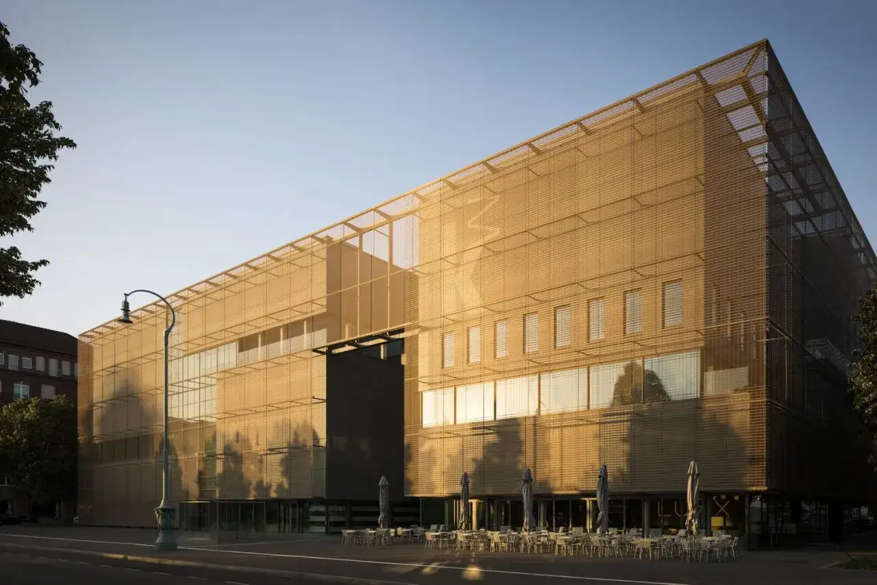 Moderne Architektur der Kunsthalle Mannheim im goldenen Abendlicht. Vor dem Geb&auml;ude laden Tische und Sonnenschirme zum Verweilen ein.