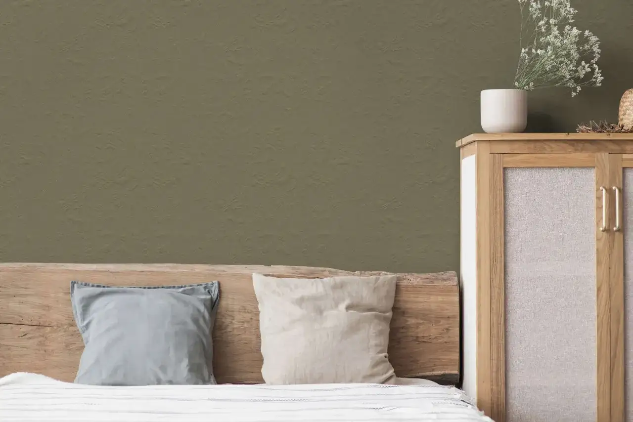 Ein Schlafzimmer mit einer Wand in einem warmen Oliv-Ton, der sich vom helleren Khaki-Kissen abhebt. Ein Holzkopfende und ein Schrank mit Stoffeins&auml;tzen vervollst&auml;ndigen den Look.