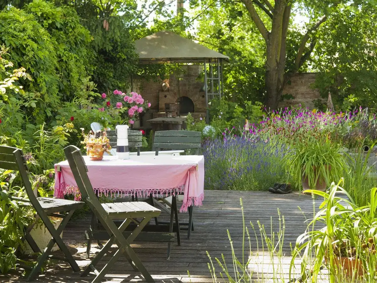 Einladende Gartenecke mit Tisch und St&uuml;hlen, umgeben von bl&uuml;henden Rosen und Lavendel. Perfekt, um eine schattige Ecke im Garten zu gestalten.