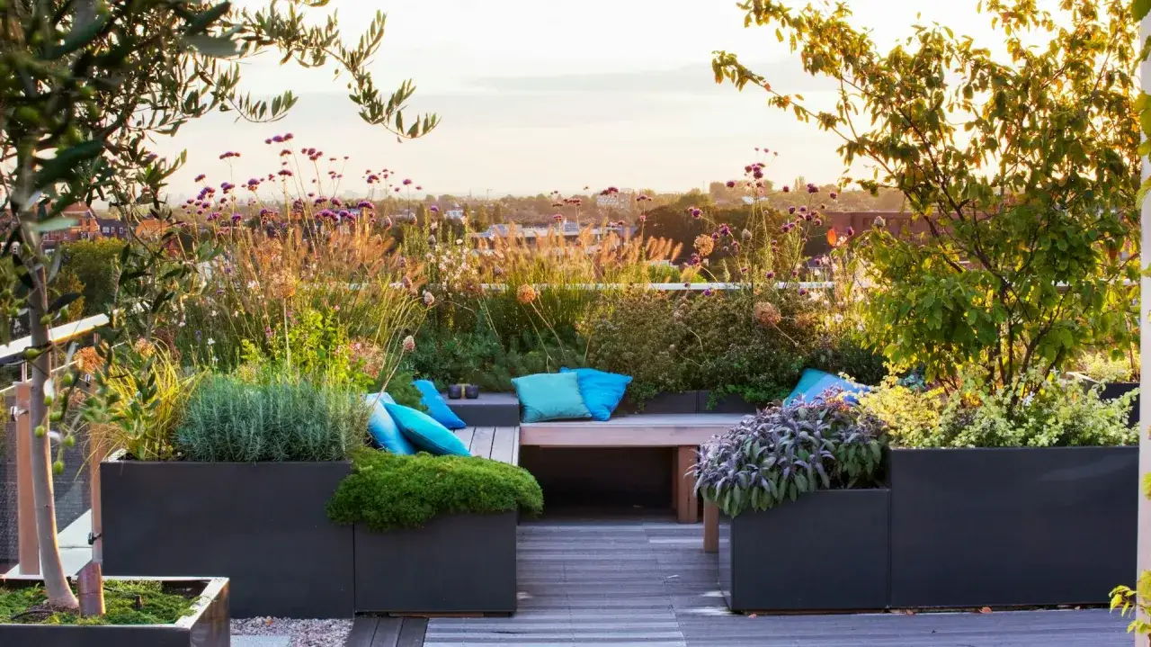 Traumhafte dachterrasse inspiration mit üppigen Pflanzen, Sitzbank und blauen Kissen, Blick über die Stadt im Abendlicht.