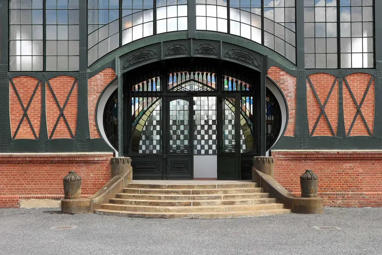 Eingang im artdeco stil mit Ziegelmauerwerk, großen Fenstern und einer kunstvollen Metalltür mit Buntglas.
