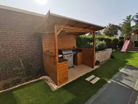 Ein moderner Grillplatz im Garten mit überdachter Holzkonstruktion, Gasgrill und gemütlicher Beleuchtung. Perfekt für Sommerabende.