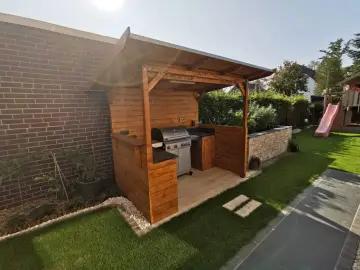 Ein moderner Grillplatz im Garten mit überdachter Holzkonstruktion, Gasgrill und gemütlicher Beleuchtung. Perfekt für Sommerabende.
