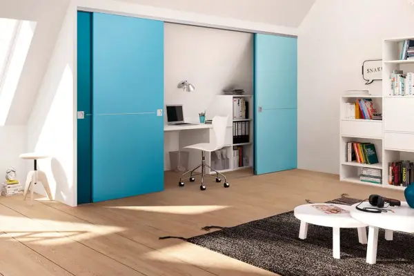 Ein kleines Arbeitszimmer einrichten: Blaue Schiebetüren verbergen einen Schreibtisch mit Laptop und Bürostuhl. Bücherregale und ein Couchtisch ergänzen den Raum.