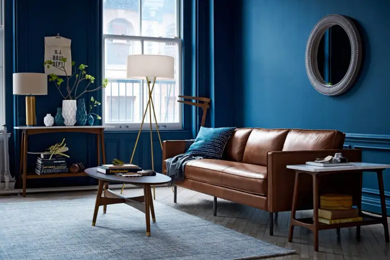 Ein Wohnzimmer mit braunem Ledersofa und blauen Wänden. Das Braun ist die perfekte gegenfarbe von braun, die dem Raum Tiefe verleiht.